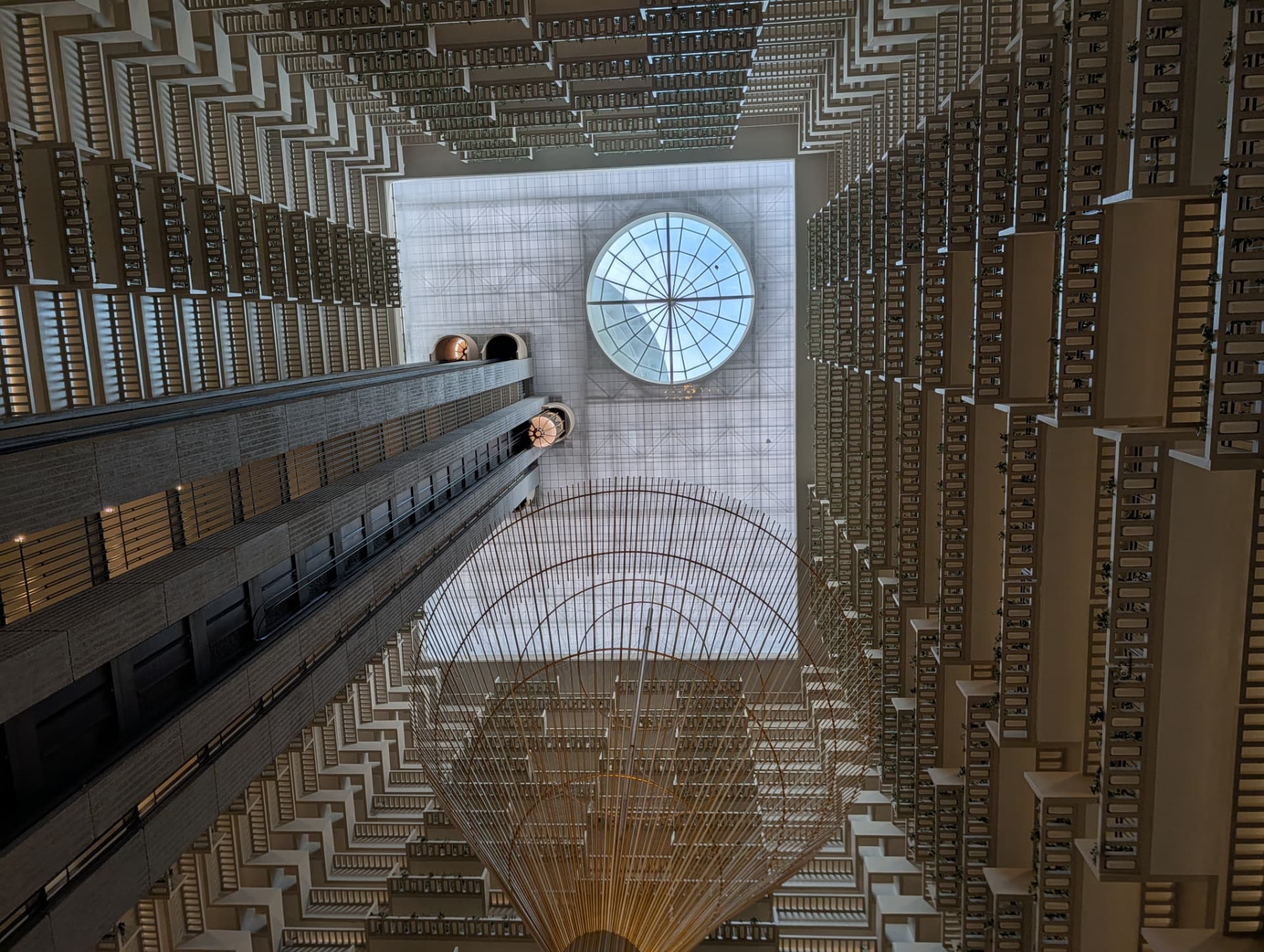 Looking up through a dramatic modern atrium with balconies, skylight, and a suspended sculpture